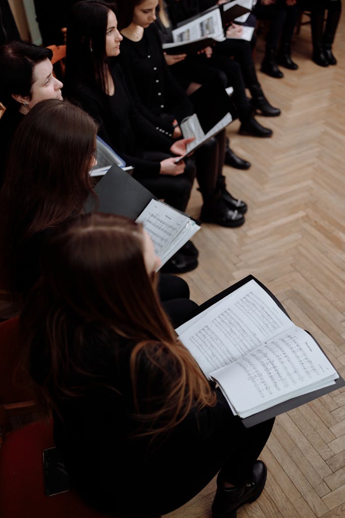 A group of women in black clothing rehearsing with sheet music in an indoor setting.